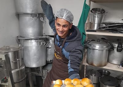 Photo of a happy cook showing a tray of bread rolls he made in a new kitchen built from a grant by The Prem Rawat Foundation