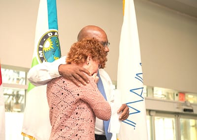 Photo of Lucy Collins, a Peace Education facilitator at the podium with Terrence Matthews of Miami-Dade Corrections and Rehabilitation Department. Terrence gives Lucy a hug as she receives her Reentry Volunteer of the Year Award.