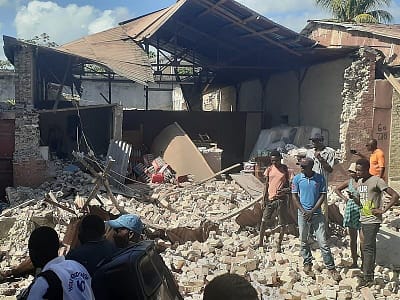 The Prem Rawat Foundation will help earthquake and flood victims in Haiti like the people pictured here in the rubble of a collapsed home.