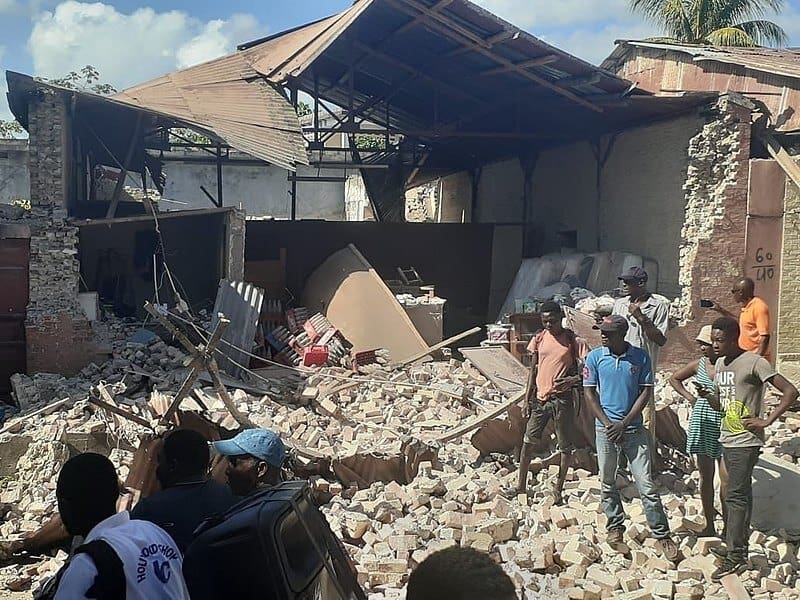 Die Prem Rawat Foundation hilft Erdbeben- und Flutopfern in Haiti, wie den hier abgebildeten Menschen vor den Trümmern eines eingestürzten Hauses.
