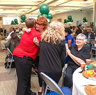 Photo of Lucy Collins, Peace Education Program facilitator, is hugging a woman in red next to a dining table at the award breakfast after receiving the Reentry Volunteer of the Year award from Miami-Dade Corrections and Rehabilitation Department