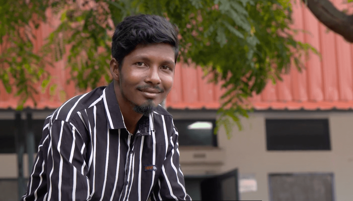 Pankaj Smiling Outside FFP Bantoli copy Pankaj dressed for work in a black shirt with white stripes and a smile, sits outside the Food for People facility in Bantoli India