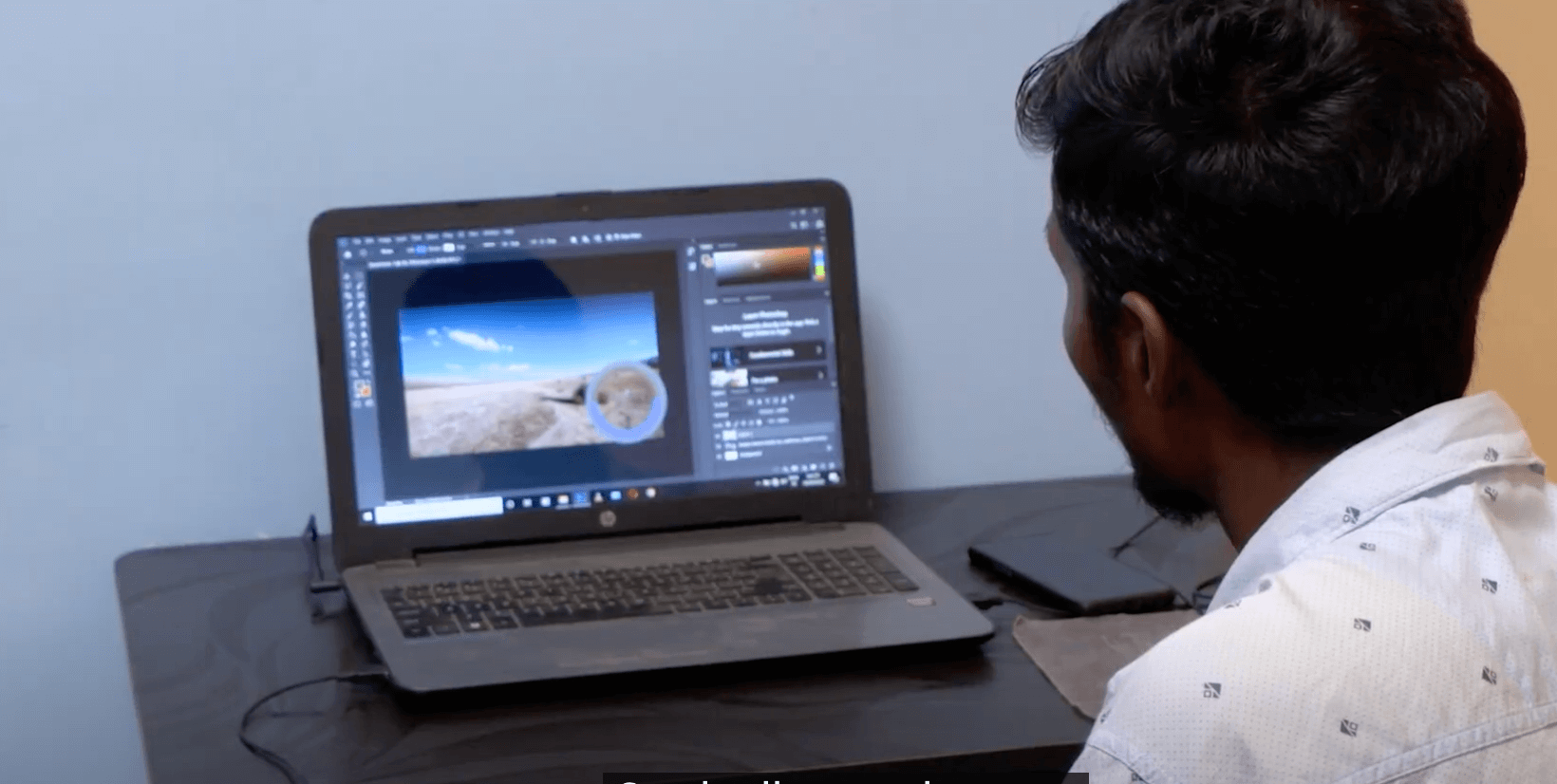 Pankaj, in camicia bianca, siede alla scrivania mentre lavora su un computer portatile