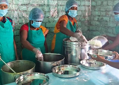 A young schoolgirl brings her shiny new meal tray to a woman who serves her rice from a spotless food serving table.